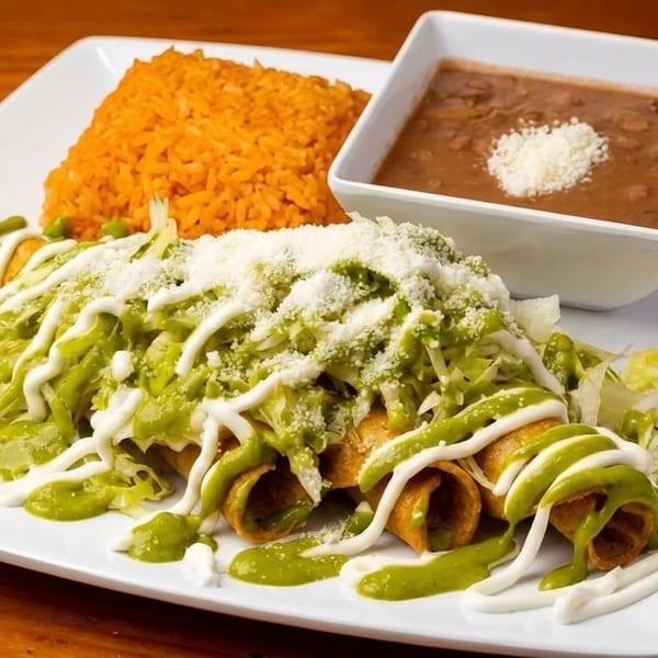 Crispy taquitos topped with green sauce, crema, lettuce, and cheese, served with rice and beans.